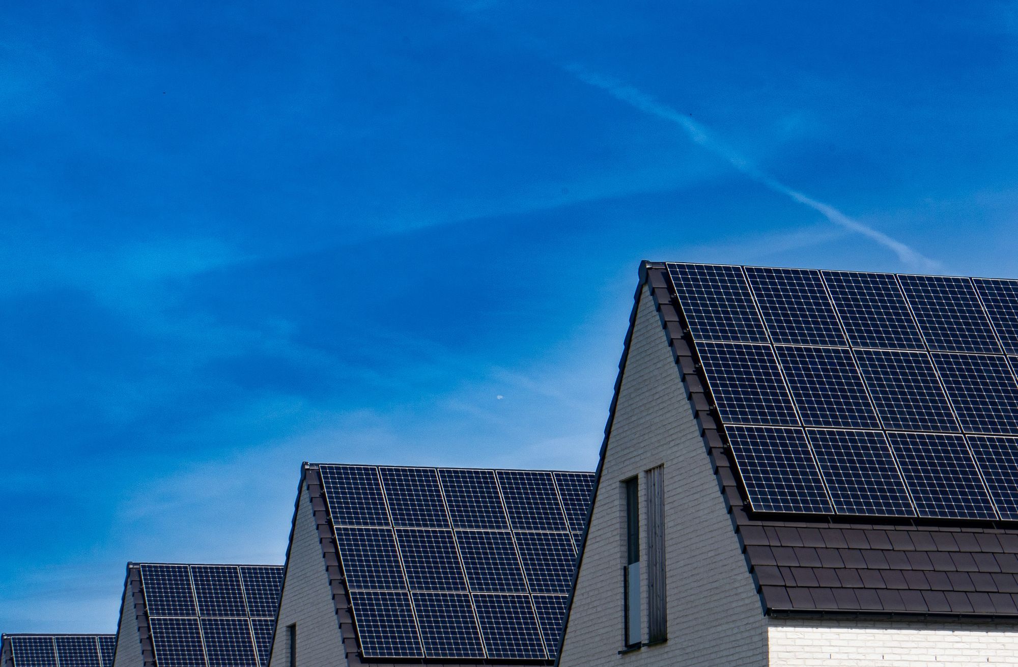 Mehrere Hausdächer mit Solarpanels vor blauem Himmel