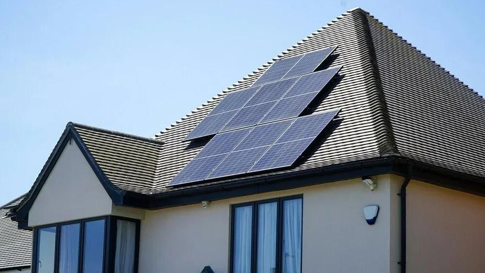 Sonnenbeschienenes Haus mit Solarpanelen am Dach vor blauem Himmel